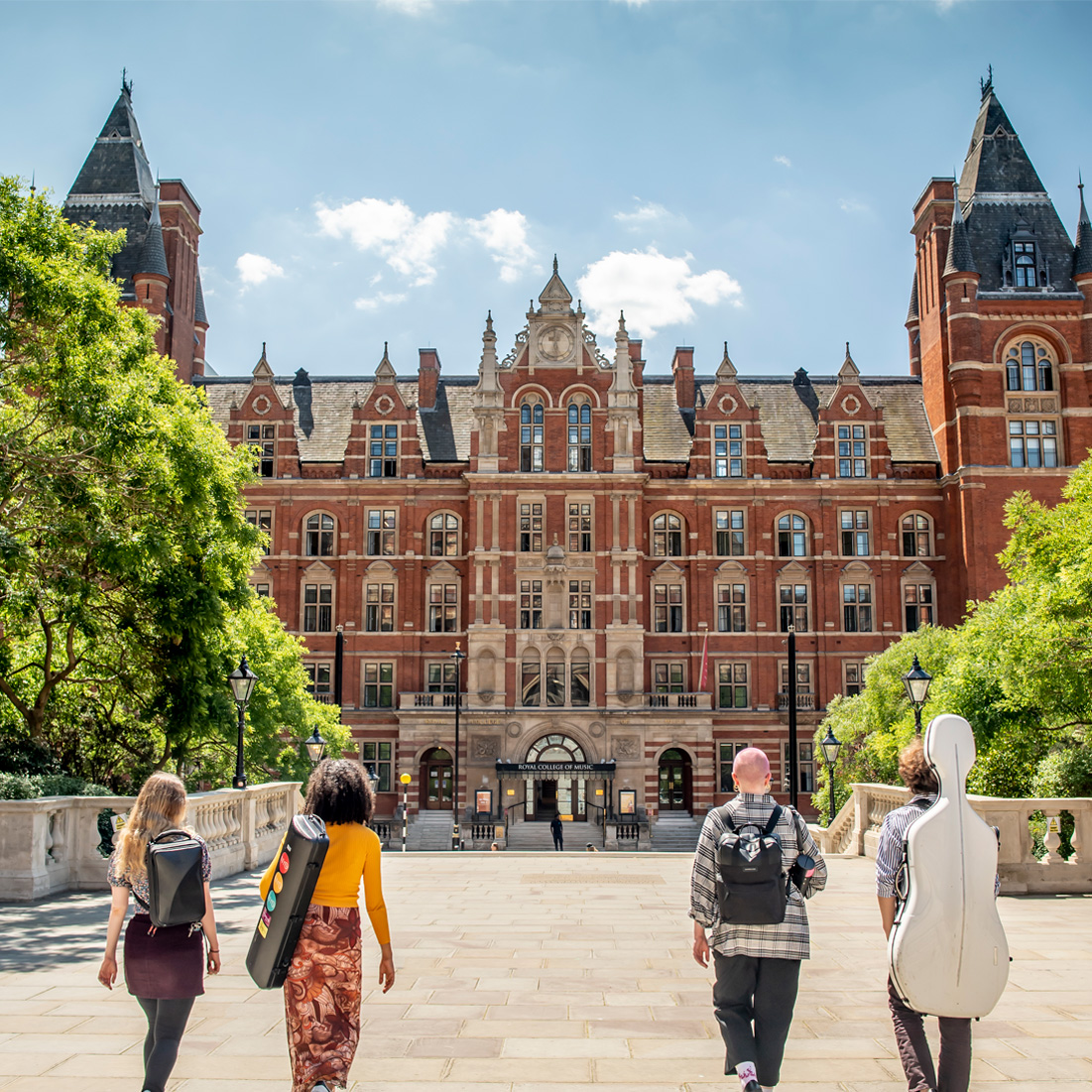 A group of students wearing casual clothes, walking towards the front entrance of the Royal College of Music, an old, red brick, Victorian building, in the background.